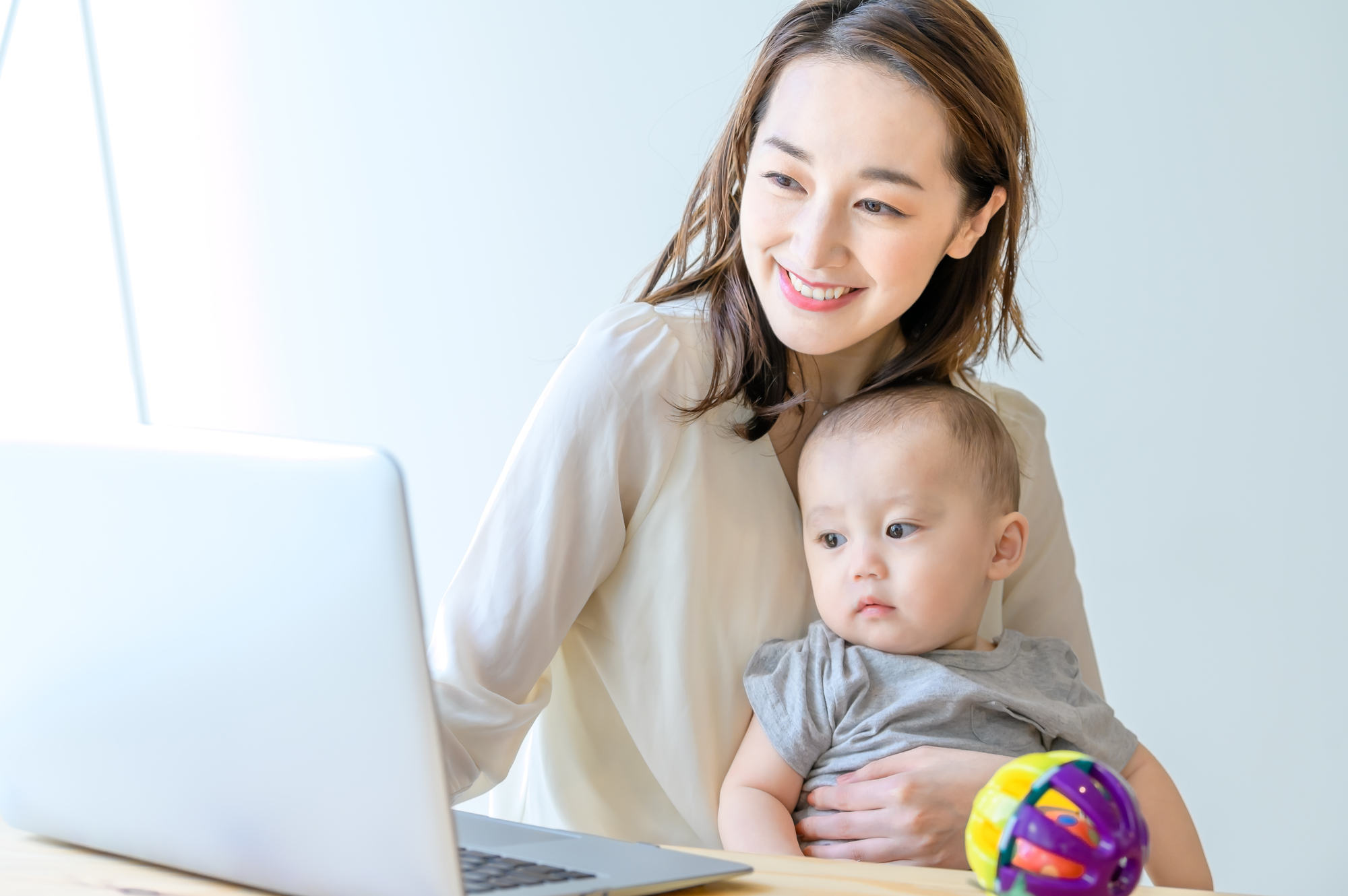 ノートパソコンの前で赤ちゃんを抱いて微笑む女性